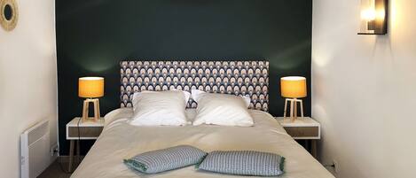 Een netjes opgemaakt bed met twee kussens, een bedlampje en een wandlamp.