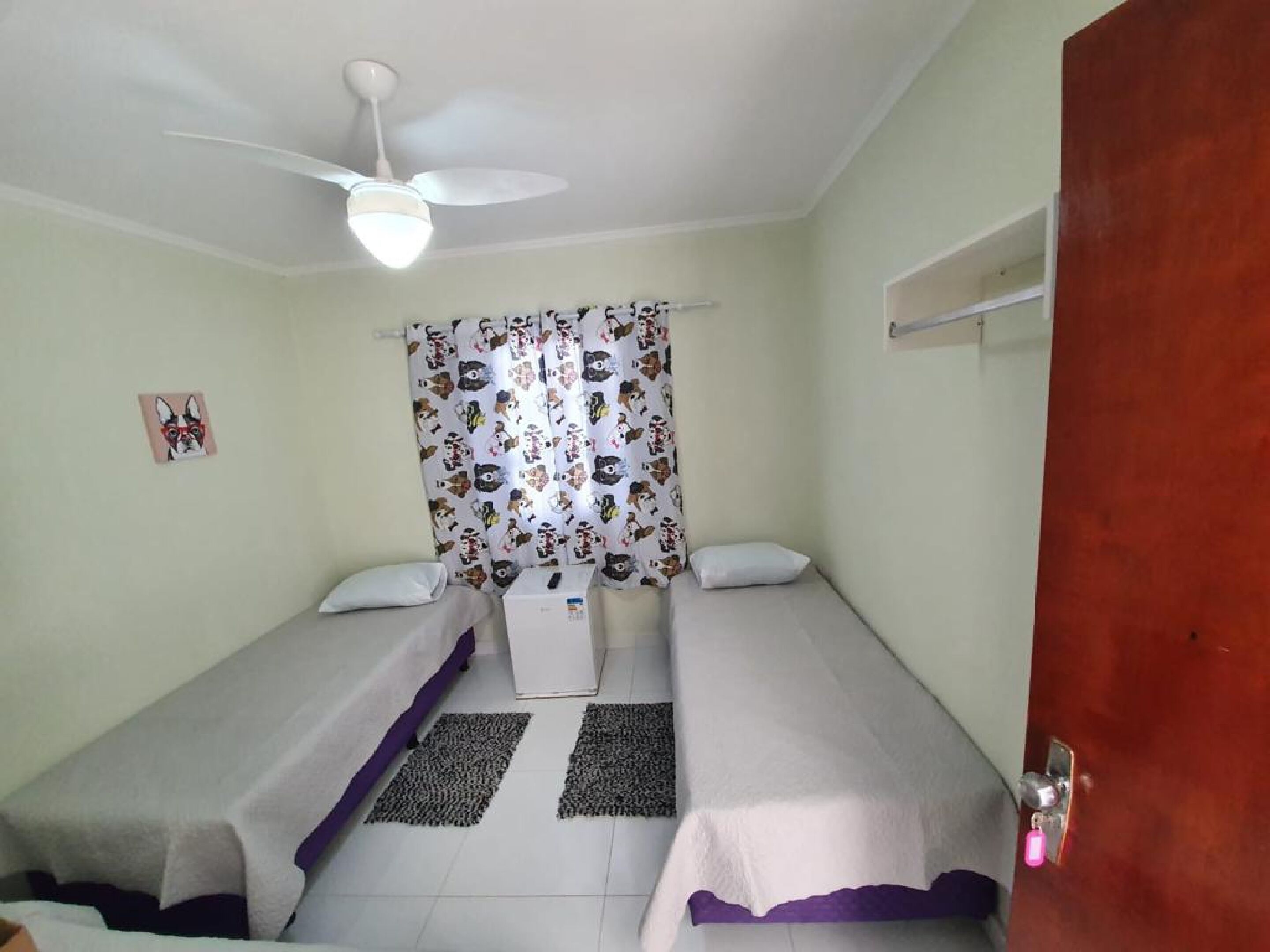 Una habitación con dos camas individuales, un ventilador de techo, una cortina de ducha con estampados de animales y un mueble blanco pequeño.