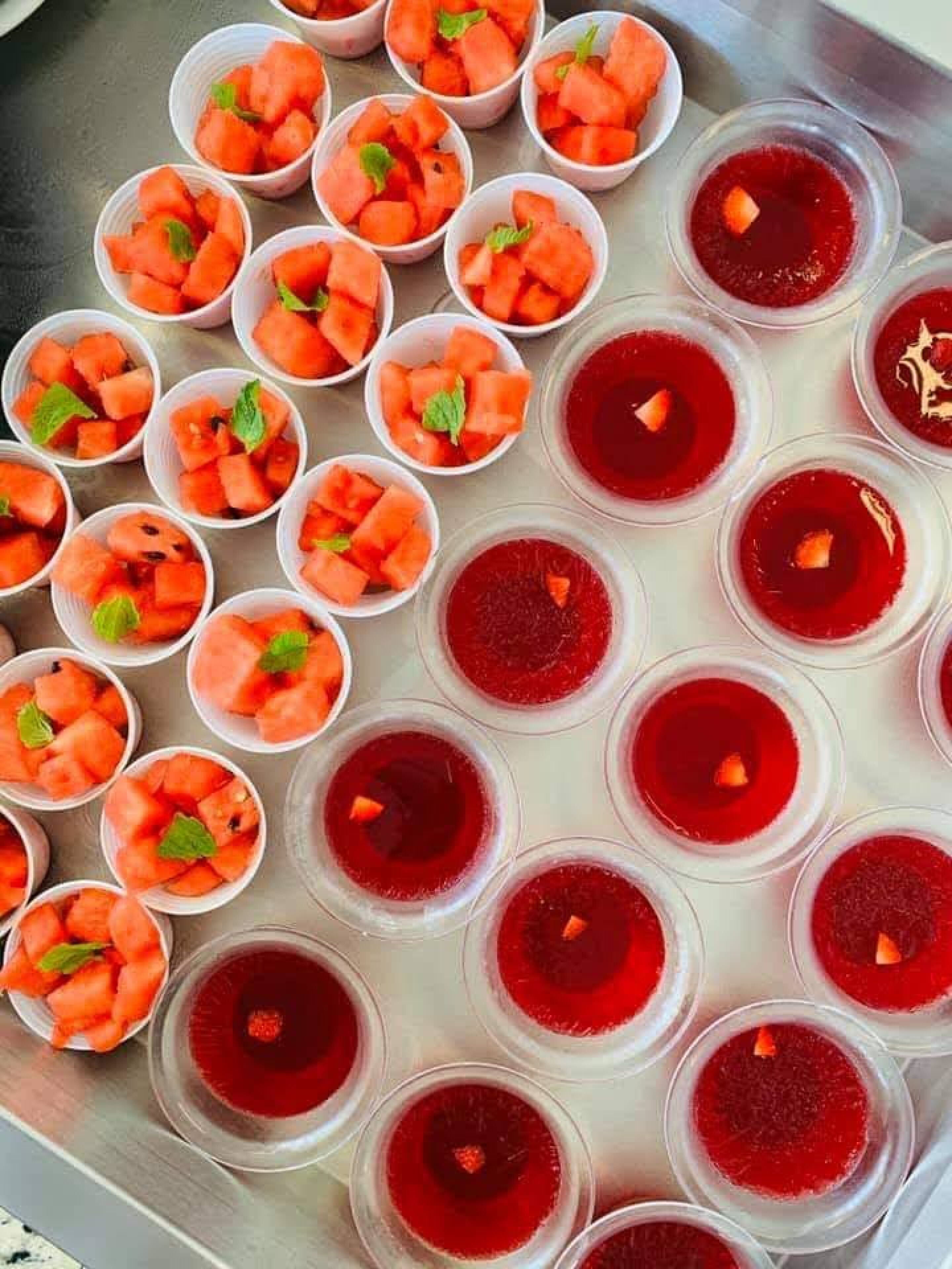 Un plateau contenant plusieurs gobelets remplis de pastèque et d’un liquide rouge, qui pourrait être une boisson ou une sauce.