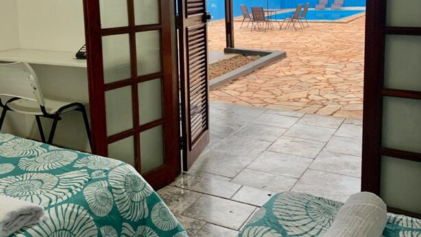 A room with a bed, a desk, and a view of an outdoor swimming pool area. - Hotel colonial lençóis Paulista (Lencois Paulista)
