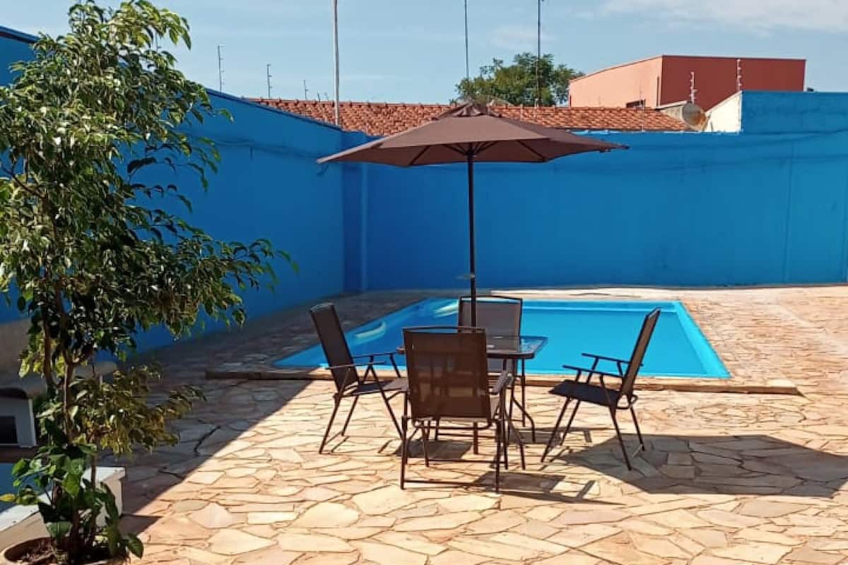 Une terrasse extérieure avec un sol en pierre, une piscine et une table entourée de chaises.