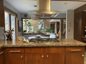 Una cocina moderna con encimeras de granito, armarios de madera, extractor de acero inoxidable y vistas a una pared de ladrillo y plantas a través de una ventana.