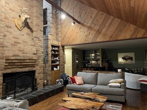 Una sala de estar acogedora con chimenea de ladrillo, techo de madera y un sofá con cojines.