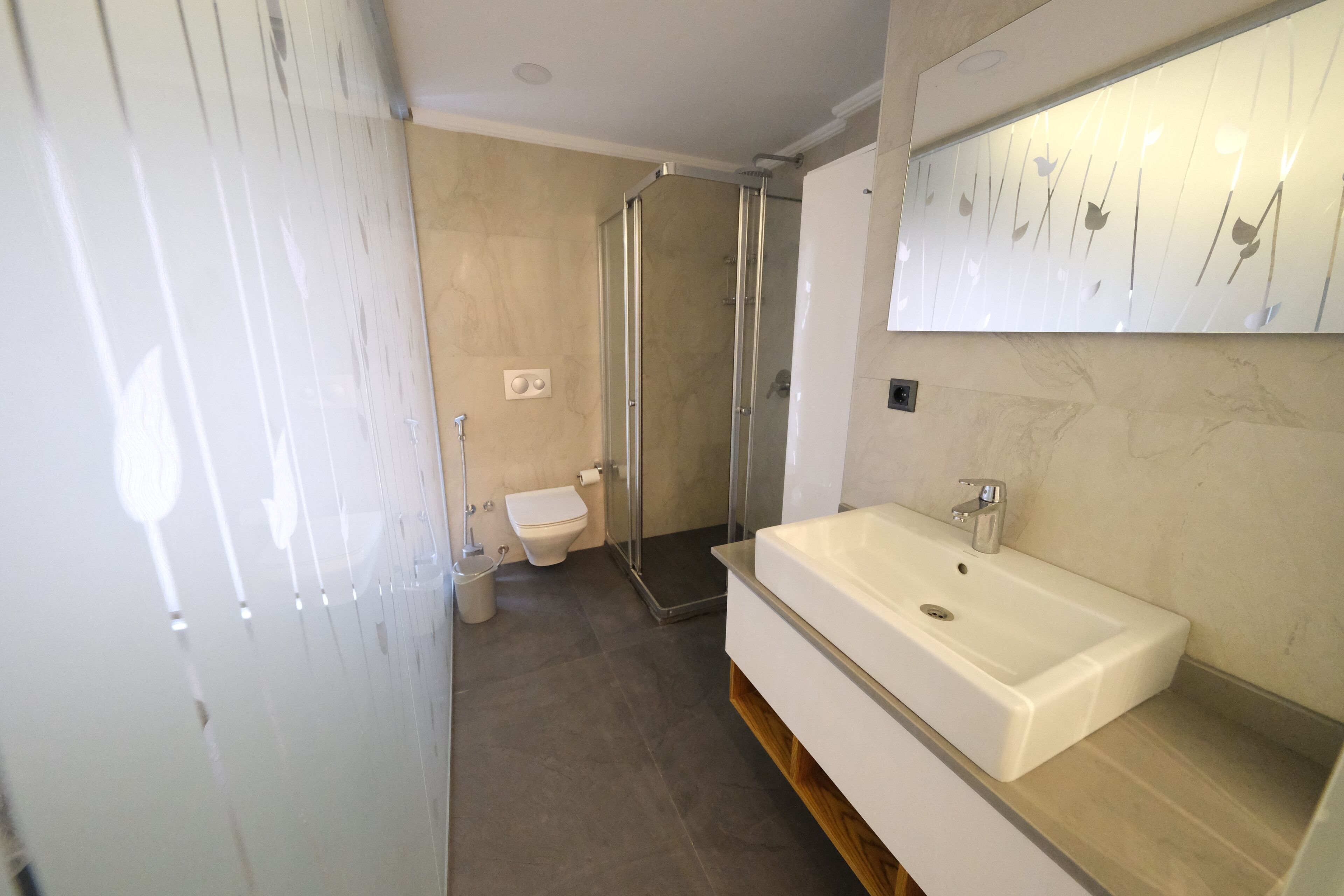 Un baño moderno con un lavamanos grande de color blanco, una cabina de ducha con paredes de vidrio y un inodoro.