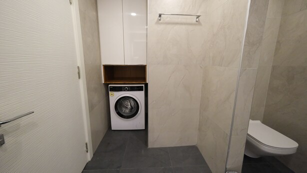 Un baño pequeño con lavadora, inodoro y un estante.