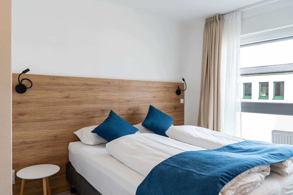 A hotel room with a wooden headboard, two blue pillows, a white bedspread, and a small white table.
