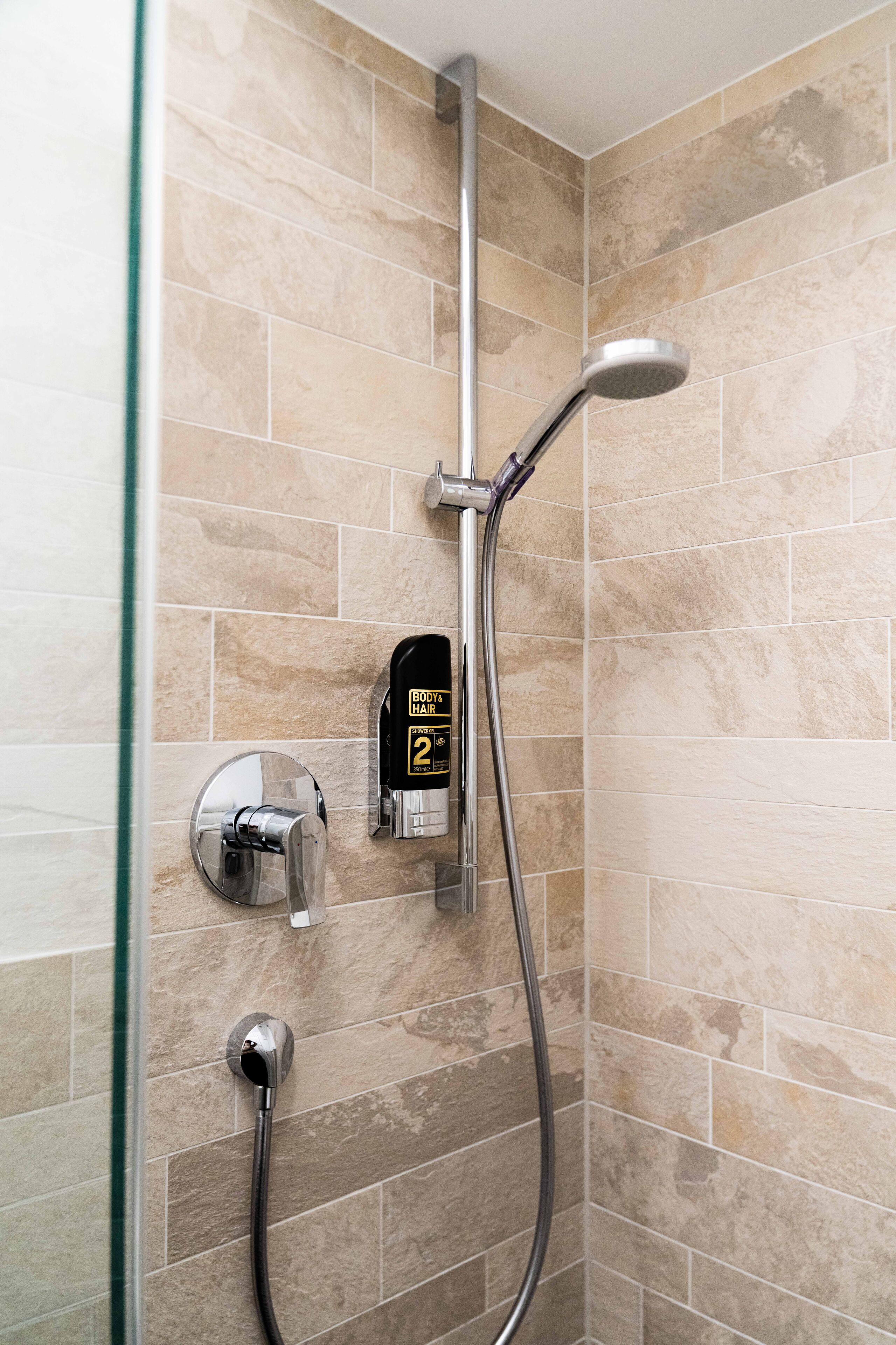 Une douche équipée d’un pommeau de douche à main, d’un distributeur de savon mural et d’un panneau de commande.