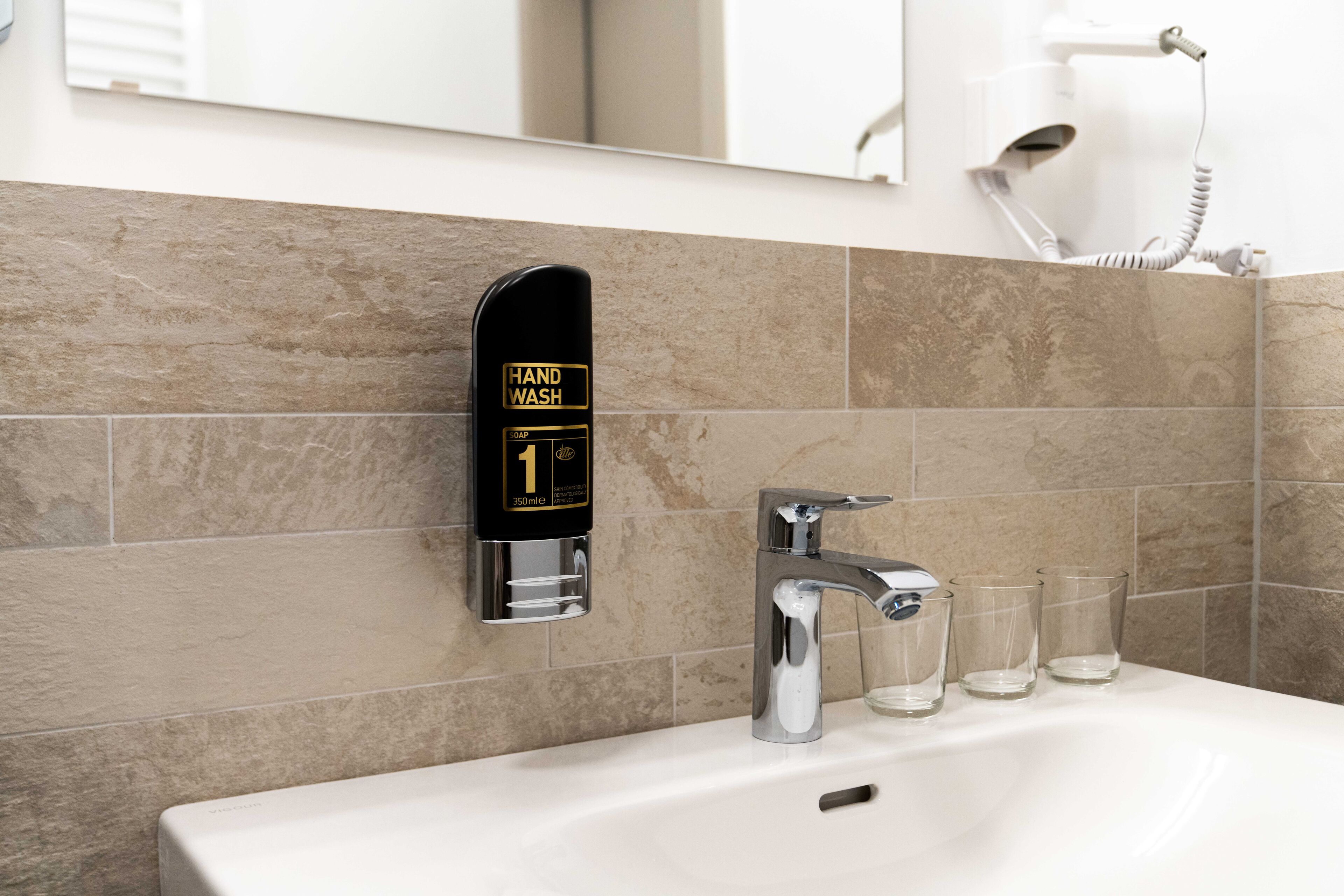 A modern bathroom with a hand wash station, a sink, and three glasses.