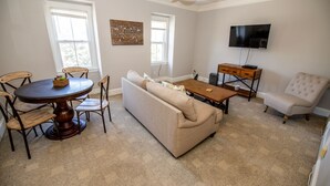Una sala de estar con una mesa redonda de madera, sofá color beige y un televisor en la pared.