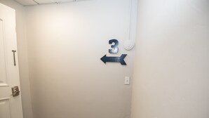 Un pasillo con pared blanca, una puerta a la izquierda y un letrero con el número 3 y una flecha apuntando a la derecha.