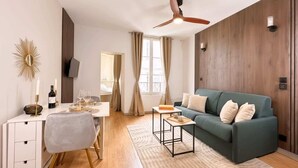 A modern living room with a sofa, a dining table, a TV, and a ceiling fan. - Stunning studio with lift - Louvre (Paris)