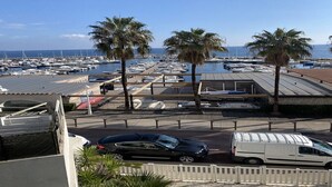 Un port de plaisance avec des bateaux, des palmiers et un espace de stationnement où sont garées des voitures et un fourgon.