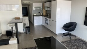 Une cuisine moderne avec des meubles blancs, une chaise noire et un coin repas doté d’une table en verre.
