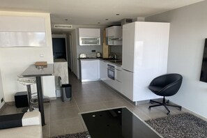A modern kitchen with white cabinets, a black chair, and a dining area with a glass table. - F2 Palm Beach - Pointe Croisette (Cannes)
