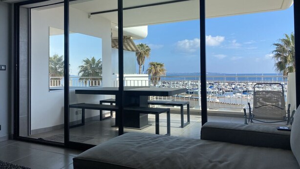 Une chambre moderne dotée d’une grande porte-fenêtre coulissante donnant sur un balcon avec vue sur une marina et des palmiers.