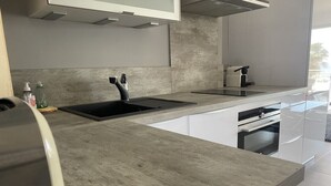 Une cuisine moderne avec un plan de travail gris, un évier noir et un four encastré.