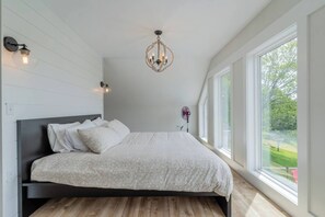 Een slaapkamer met een groot bed, een kroonluchter, een ventilator en uitzicht op de omgeving.