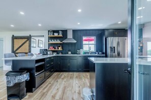 A modern kitchen with dark cabinetry, a central island, and a built-in oven. - Wentworth Private Cottage with Hot Tub (Colchester)