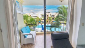 Un balcon donnant sur une piscine, avec des meubles en osier blancs et un canapé gris.