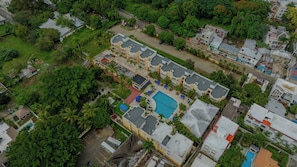 Vue aérienne d’un quartier résidentiel avec un grand immeuble doté de nombreux balcons, d’une piscine et d’un espace vert environnant.