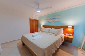 A hotel room with a bed, a nightstand, a ceiling fan, and a wall with artwork.