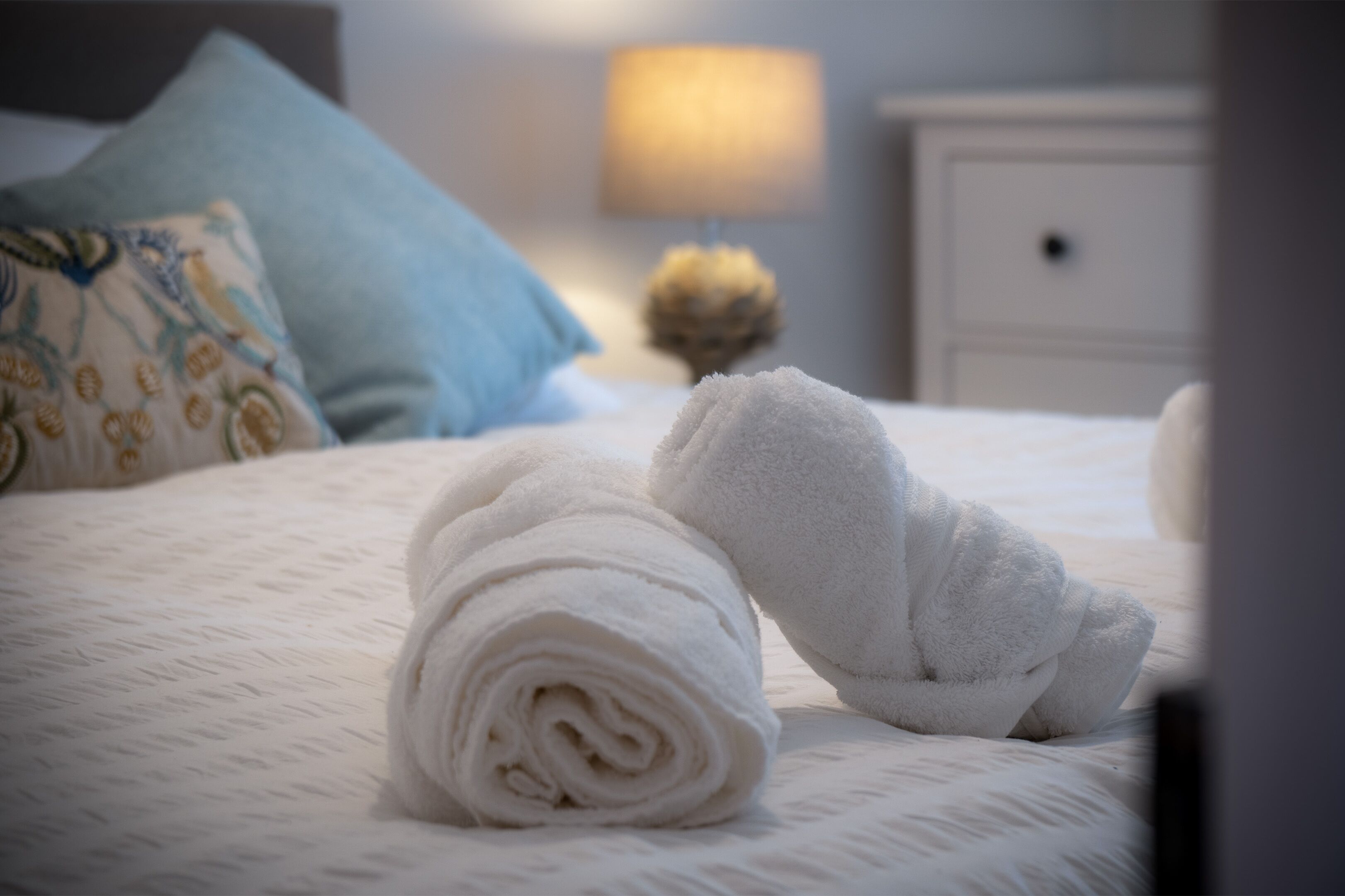 A neatly made bed with rolled white towels and a blue pillow.