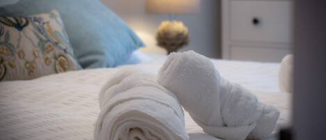 A neatly made bed with rolled white towels and a blue pillow.