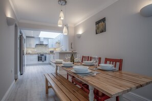 A dining area with a wooden table set for four, a bench, and a view into the kitchen.
