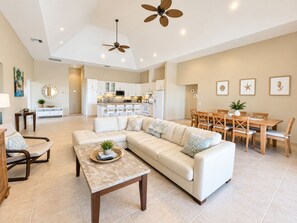 A spacious living area with a large L-shaped sofa, a dining table with chairs, and a kitchen in the background.