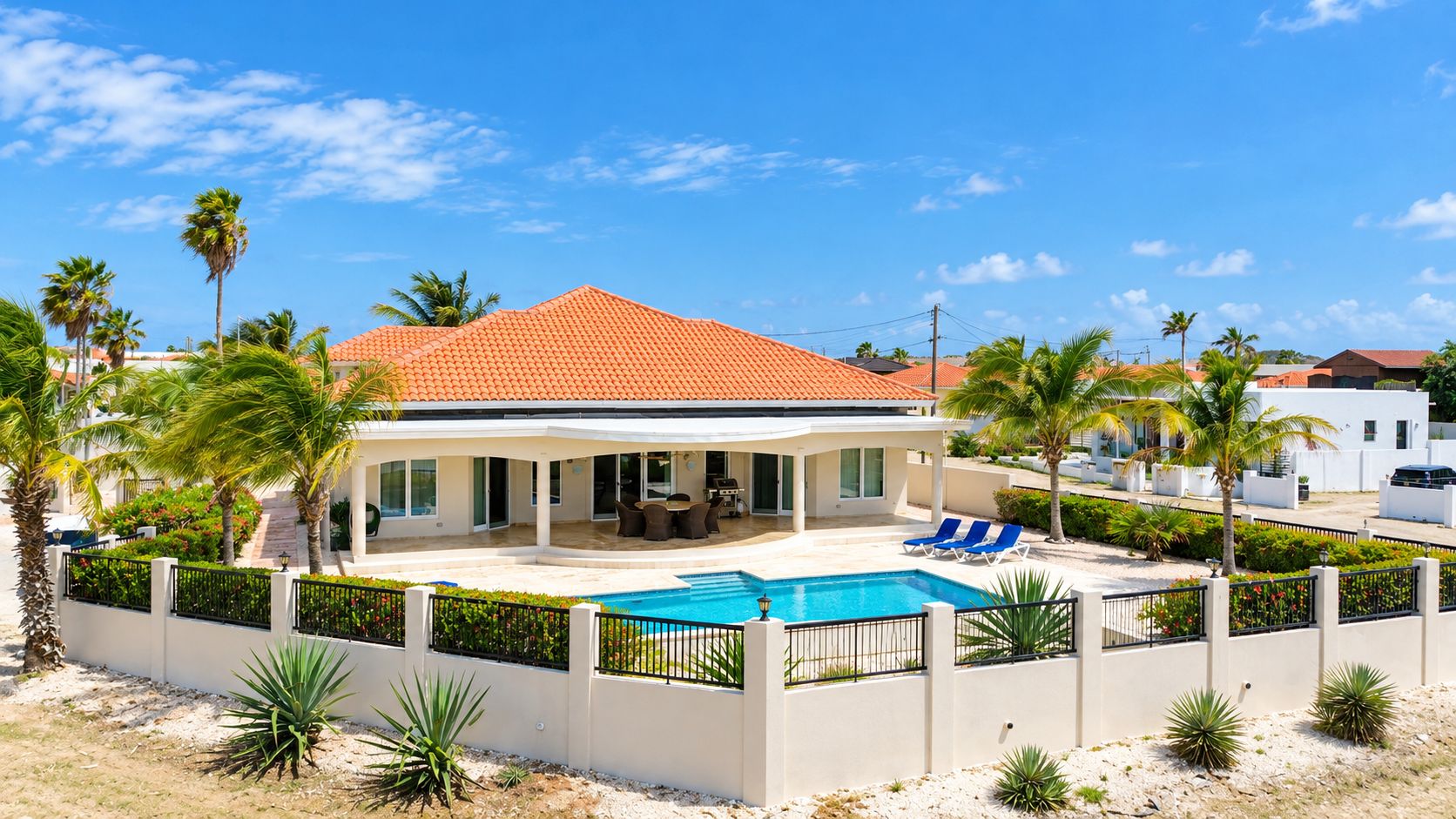 Een huis met een zwembad, overdekt terras en palmbomen.