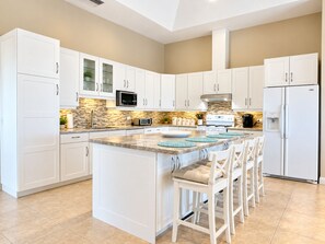 A modern kitchen with white cabinets, a central island with bar stools, a microwave, a stove, and a refrigerator. - Luxury Ocean View Villa, Stunning Views, 5 minutes to Beaches (Noord)