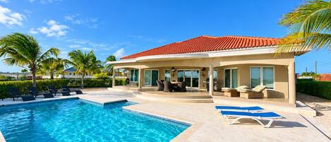 A poolside area with a house, lounge chairs, and a clear blue sky.