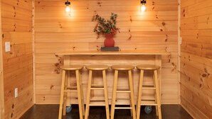 A wooden interior with a bar area featuring a red vase with flowers, two hanging light fixtures, and three stools.