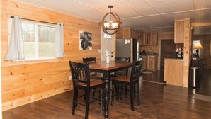 A wooden-paneled room with a dining table and chairs, a chandelier, and a kitchen area with cabinets and appliances.