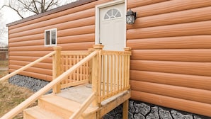 A wooden cabin with a front door, a small window, and a wooden staircase leading up to the door.