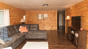 A cozy living room with a sectional sofa, a flat-screen TV, and a wooden wall panel.