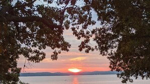 A wooden deck with a table and chairs overlooking a calm body of water during sunset. - Small rustic cabin on KY Lake (sleeps 4) (New Concord)