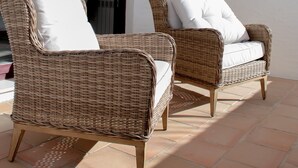 Two wicker chairs with white cushions on a tiled patio.