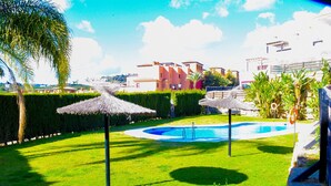 A pool area with thatched umbrellas, a well-maintained lawn, and a building in the background.