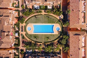 Vue aérienne d’un complexe hôtelier doté d’une piscine centrale, entouré de palmiers et d’une allée circulaire.