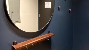 Um banheiro com um espelho redondo, uma prateleira de madeira e uma porta com um pequeno vitral.