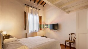 A bedroom with a bed, a chair, a TV mounted on the wall, and a window with curtains. - Canacci by Mmega (Florence)