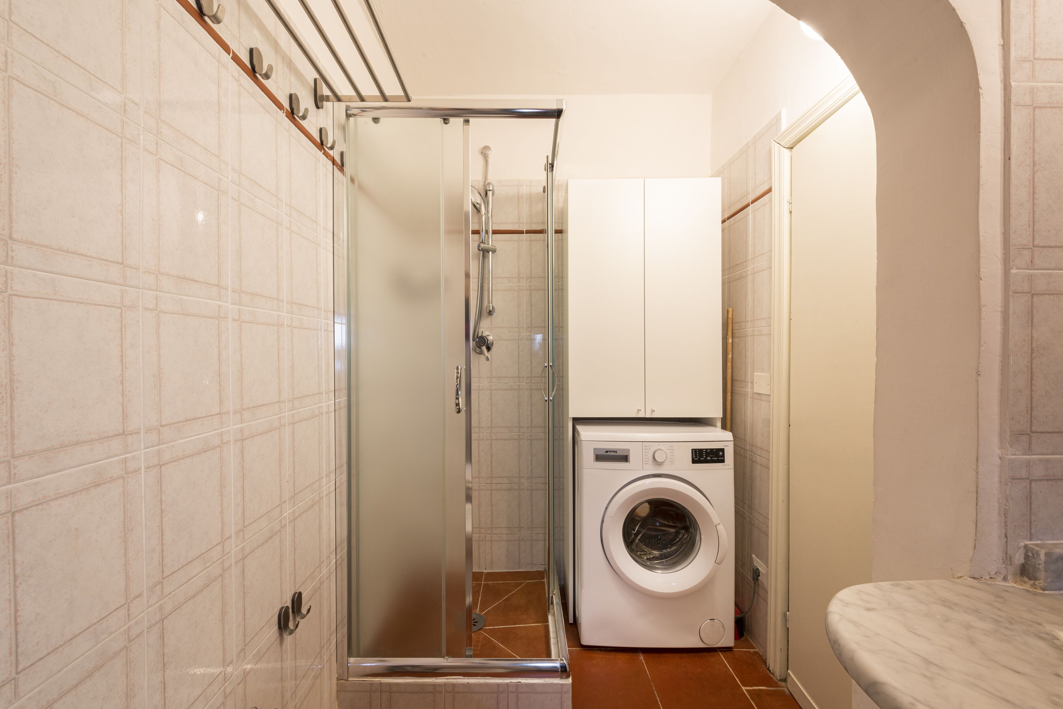A compact bathroom with a glass shower enclosure, a washing machine, and a toilet.