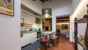 A compact kitchen with white cabinets, a black stove, and a dining area with a red chair and a green chair. - Canacci by Mmega (Florence)