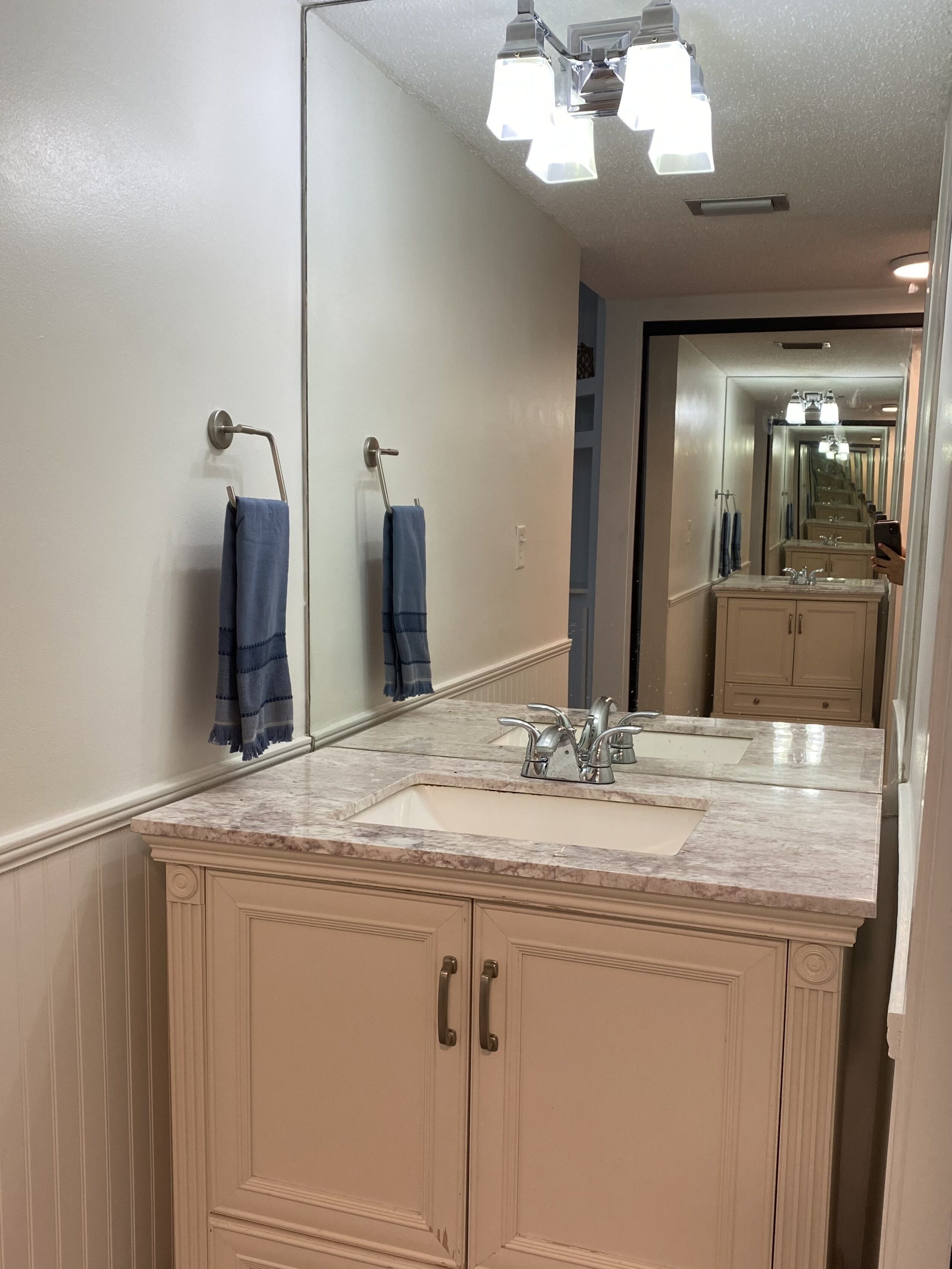 A bathroom with a large mirror, a sink with a marble countertop, and beige cabinetry.