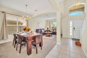 A spacious living area with a dining table, sofas, and a staircase leading to an upper level.