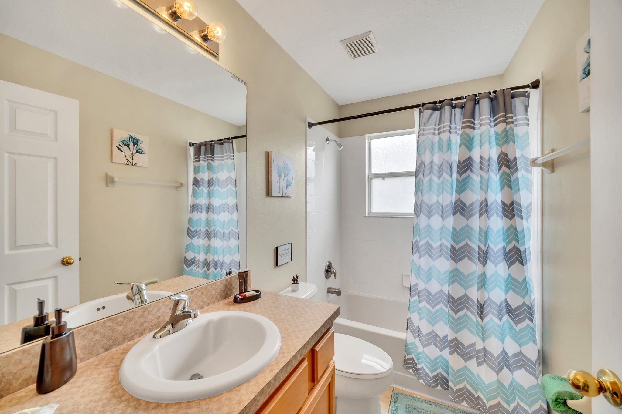 Une salle de bain équipée d’un lavabo, d’un miroir, d’une douche et d’une fenêtre avec un rideau de douche.