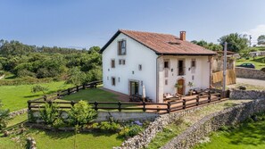 Una casa bianca a due piani con tetto in tegole, circondata da un muro in pietra e una recinzione in legno.