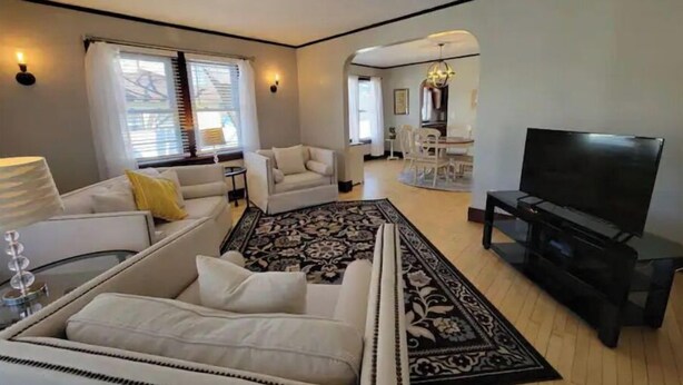 A modern living room with a sofa, a TV, and a dining area in the background. - SPACIOUS BUNGALOW- 20min to WI Dells/Devils Lake (Portage)