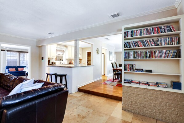 A living room with a leather sofa, a bookshelf, and a kitchen area in the background.